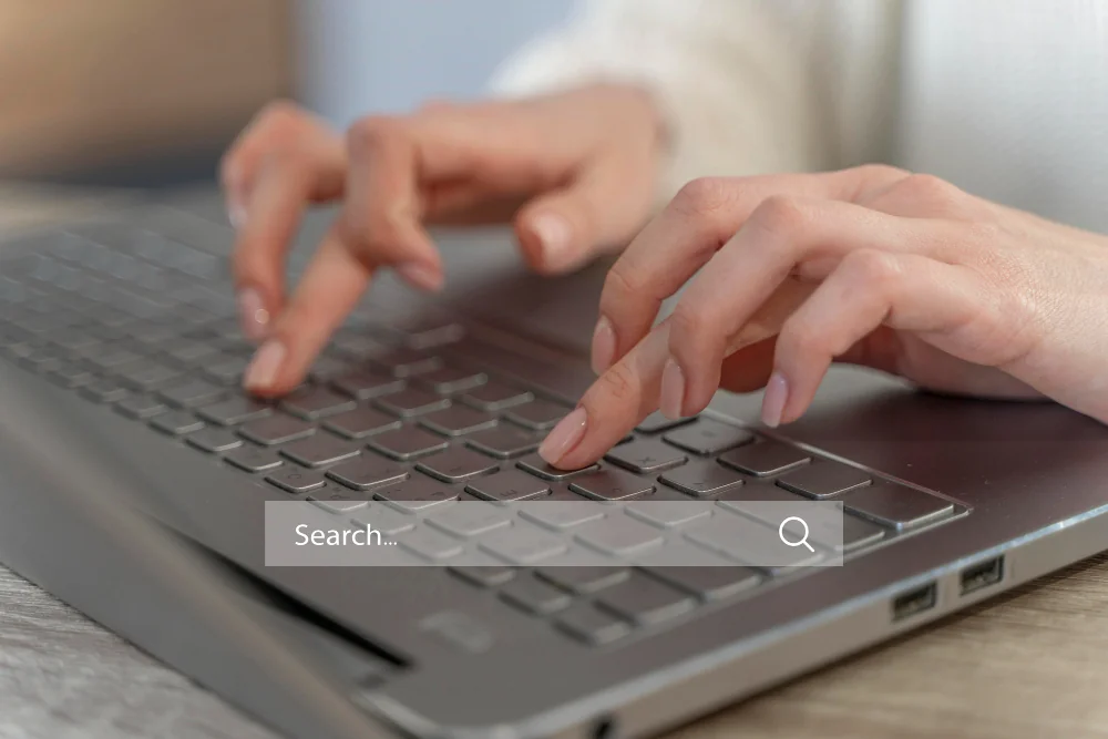 A person types on a laptop keyboard with a search bar overlayed at the bottom of the image.
