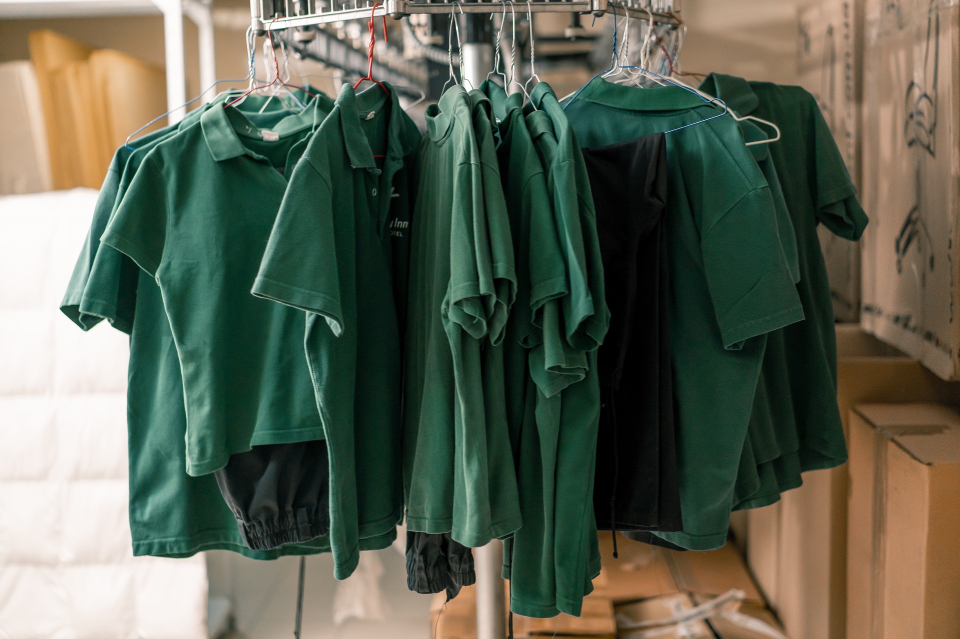 A rack of green polo shirts and black shorts hanging on hangers in a storage or laundry room.