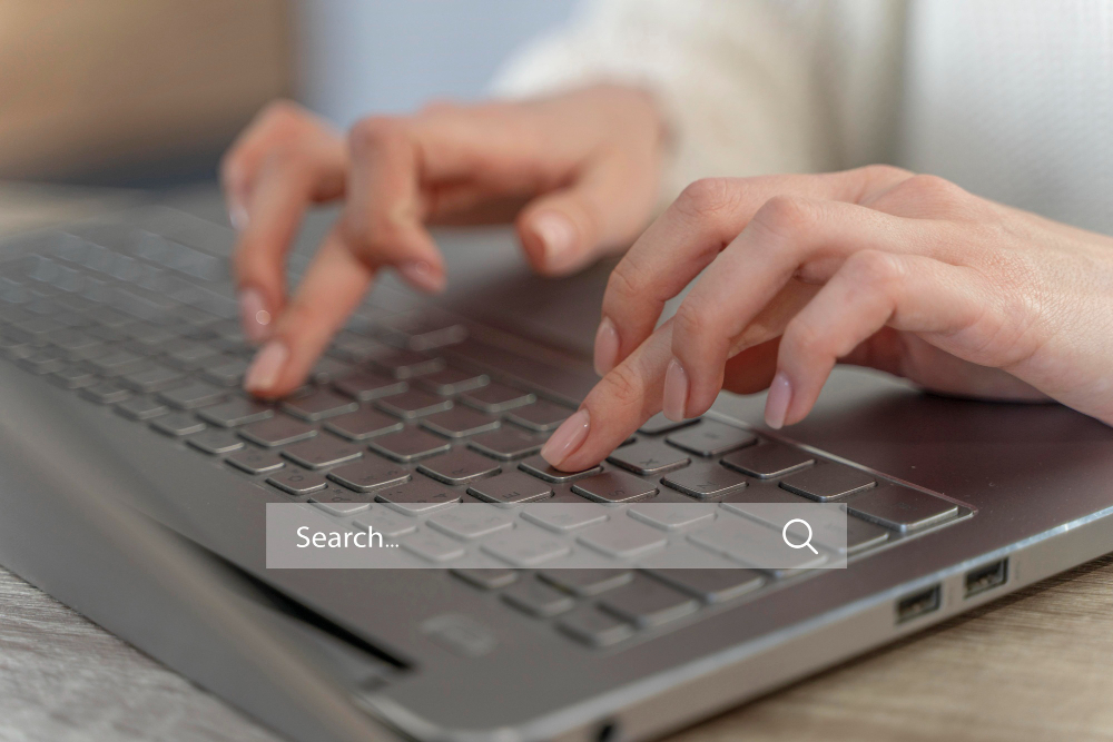 A person types on a laptop keyboard with a search bar overlayed at the bottom of the image.