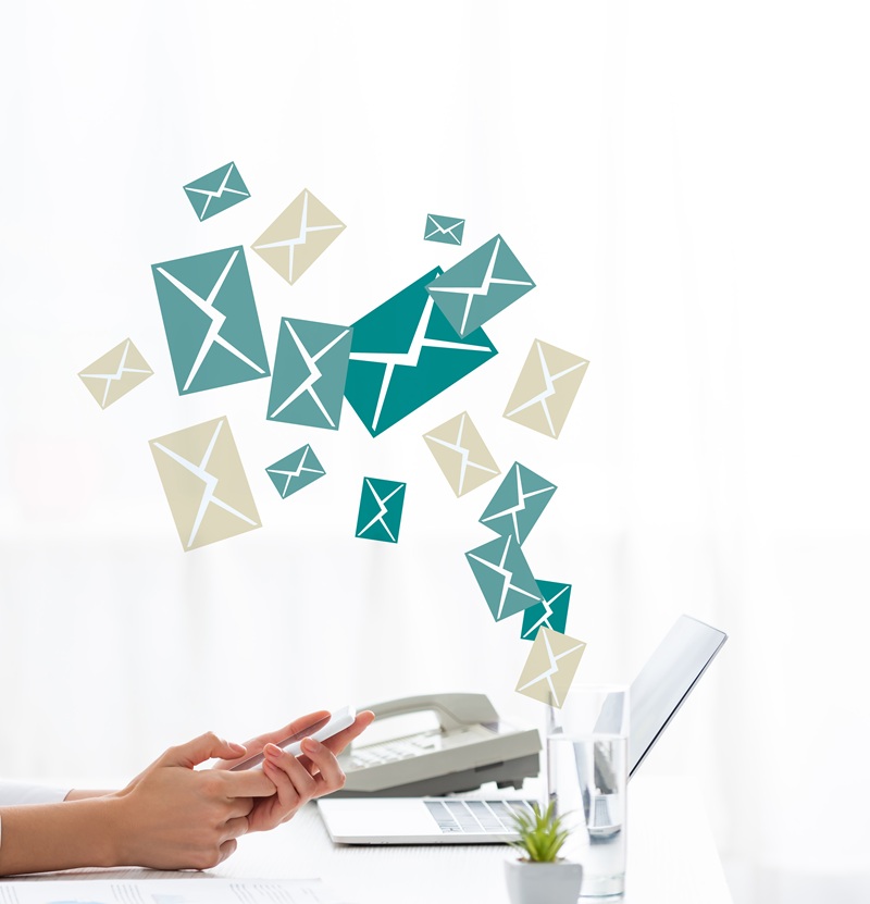 Person using a laptop with illustrated envelopes floating above, symbolizing receiving or sending multiple emails; office items and a plant are visible in the background.